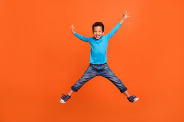 Fototapeta na wymiar Full size photo of charming little schoolboy jumping high excited back school wear trendy blue garment isolated on orange color background