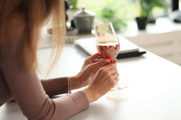 Female hands holding a glass of red wine, close up shot with selective focus. Drink in hands against the backdrop of a bright kitchen
