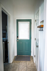 A dark teal painted interior back door inside an Acadian style Louisiana home with tile floors and hooks to hang jackets on the wall