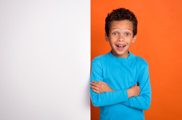 Photo portrait of cute small pupil boy impressed poster offer folded arms dressed stylish blue garment isolated on orange color background
