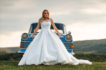 Beautiful bride posing with old vintage blue car in sunset.