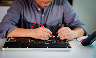 A male repairman is using a meter to measure the malfunction of a notebook computer's electronic equipment. Electronic equipment and deterioration and find a way to repair