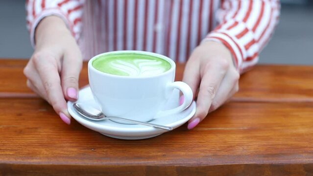 woman puts a cup of matcha latte in a coffee shop outside
