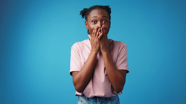 Shocked surprised young african woman against blue background