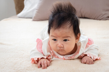 Fototapeta premium close-up of Newborn 3 month old Asian woman playing in bed in the bedroom of the house. After waking up, he looked for his mother in frustration, lowering his head and raising his head.
