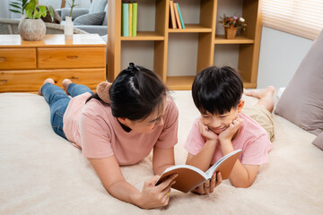 Asian mother and boy, wearing a pink t-shirt, The two of them lay comfortably on the bed, mother holding a playbook in her hand to read to his son, And the two of them play warm and cute.
