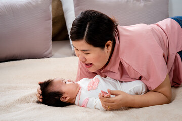 A 3 month old newborn baby is laying in bed happily. and single moms recline for comfort and play. A real mother comforts a newborn baby to sleep. on a soft mattress in the bedroom