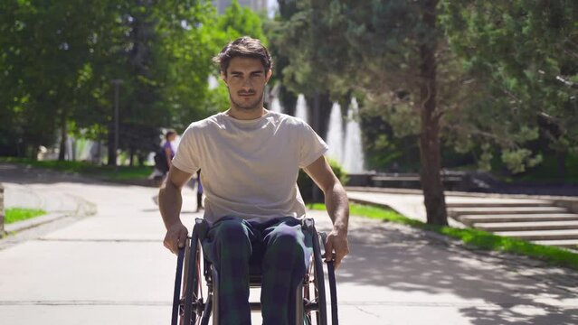 Young disabled man walking down the street with his wheelchair.
Determined young man drives his wheelchair looking at the camera.
