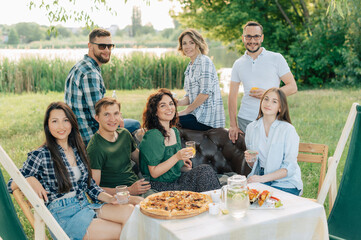 Group of friends are relaxing together outdoor. Young cheerful people clink glasses and laugh.