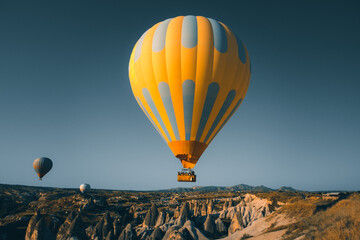 Yellow bright hot air balloon with tourists rise up for sunrise watching. Wide blue sky landscape of Goreme valley in Cappadocia. Tourism, travel, holidays, recreation background, concept postcard