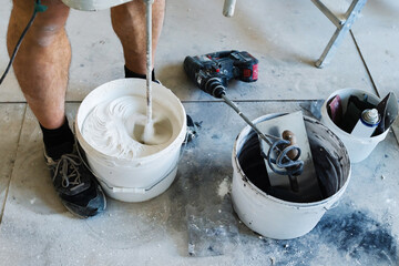 The process of kneading gypsum plaster with a power tool. A builder using a mixer prepares a mortar for puttying walls and ceilings. Close-up. unrecognizable person