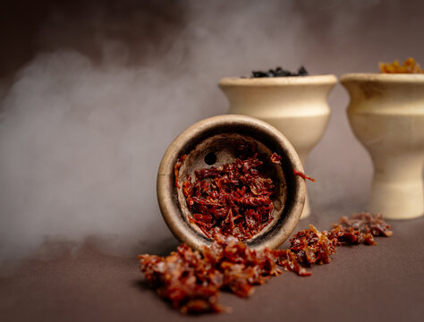 Three hookah bowls with aromatic tobacco with smoke on a brown table with smoking accessories. Hookah smoking in a hookah lounge. Red, yellow, black hookah tobacco