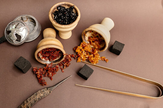 Three hookah bowls with aromatic tobacco on a brown table with smoking accessories. Hookah smoking in a hookah lounge. Red, yellow, black tobacco for hookah, charcoal, tongs