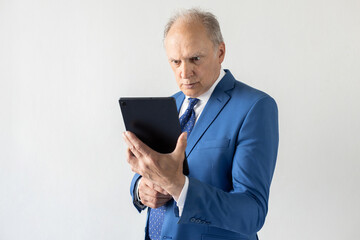 Portrait of worried mature businessman using digital tablet. Concentrated senior manager wearing formalwear reading information on touchpad against white background. Bad news concept