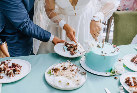 The bride and groom cut the sweet, delicious wedding cake, which is on the table, into a piece with a knife at the ceremony. Photography, dessert.