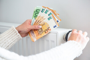 Saving home heating, expensive payment for heating. Radiator and euro money banknotes in woman hands.