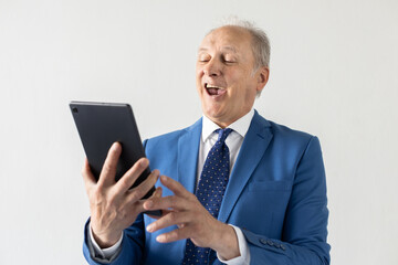 Portrait of mature businessman using digital tablet and laughing. Senior manager wearing formalwear watching funny video on touchpad against white background. Wireless technology concept