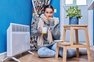 Female in warm sweater scarf warming near electric heating radiator