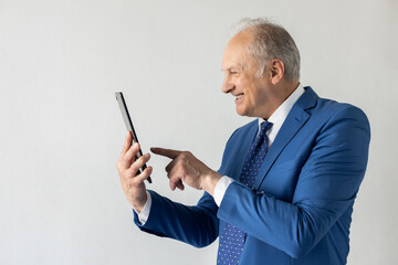 Side view of positive mature businessman using digital tablet. Senior manager wearing formalwear reading news on touchpad and laughing against white background. Wireless technology concept