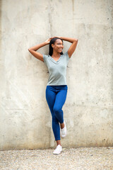 Fototapeta premium Happy black woman looking away while leaning against wall with hands behind head