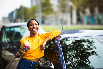 Happy black woman leaning on her new car and showing the keys