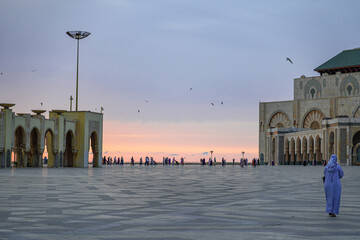 Mezquita de Hassan II en Casablanca Marruecos, mujer arabe paseando  con kaftan azul y familias paseando en el atardecer  .