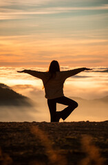 Fototapeta premium Silueta de chica haciendo pose de yoga de fondo mar de nubes en el atardecer .