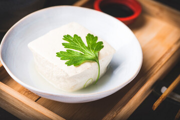 Fresh tofu japanese soy cheese whole piece with the paracley leaves on ceramic azure plate with chopsticks over wooden vintage table,  dark key, close up. Autumn and winter hot Japanese recipe