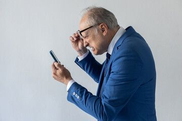 Portrait of outraged mature businessman reading message on phone. Senior manager wearing formalwear taking off glasses and looking at smartphone in surprise. Astounding news concept