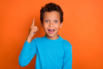 Photo portrait of charming small boy finger point up excellent idea dressed stylish blue garment isolated on orange color background