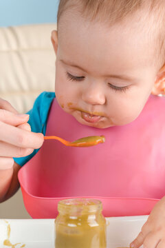 Mom feeds baby 12-17 months with a spoon of green vegetable puree, vertical photo