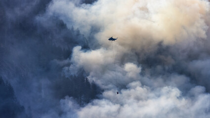 Wildfire Service Helicopter flying over BC Forest Fire and Smoke on the mountain near Hope during a hot sunny summer day. British Columbia, Canada. Natural Disaster