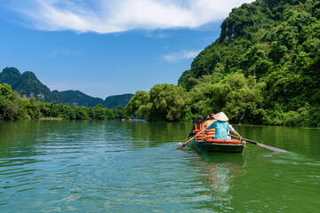 Tourists sitting on rowing boats enjoy the beautiful scenery of rivers and mountains in Trang An, Ninh Binh province, Vietnam. © ducvien