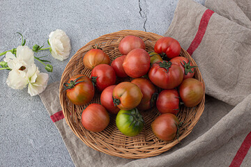 fresh red tomato on wicker basket on gray background.