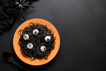 Italian black pasta squid ink decorated horror eyes in orange plate for Halloween party on black...