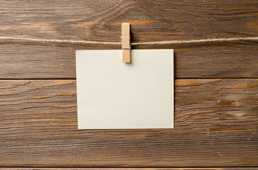 An empty piece of paper is hanging on a rope. A design element. Brown wooden background. Copy space.