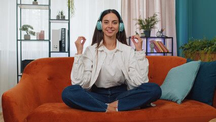 Obraz premium Keep calm down, relax, inner balance. Adult girl breathes deeply with mudra gesture, eyes closed meditating with concentrated thoughts, peaceful mind. Young woman sit at home in living room on couch