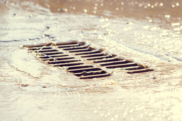 The grate of the storm sewer after the rain. The water drains into the storm drain. Selective focus, defocused background