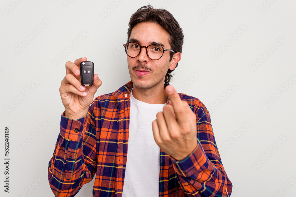 Wall mural Young hispanic man holding car keys isolated on white background pointing with finger at you as if inviting come closer.