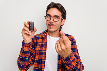 Young hispanic man holding car keys isolated on white background pointing with finger at you as if inviting come closer.