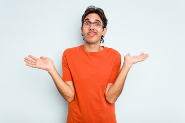 Young hispanic man isolated on blue background doubting and shrugging shoulders in questioning...