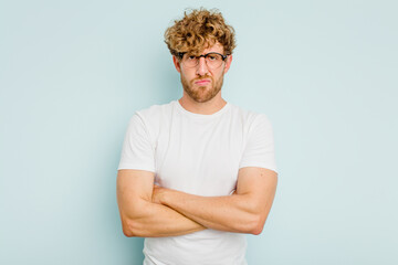 Young caucasian man isolated on blue background frowning face in displeasure, keeps arms folded.