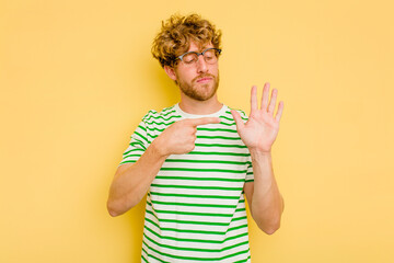 Young caucasian man isolated on yellow background smiling cheerful showing number five with fingers.