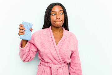 Young African American woman holding a sponge isolated on blue background  confused, feels doubtful and unsure.