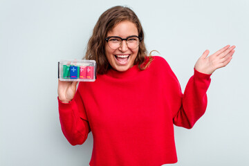 Young caucasian woman holding battery box isolated on blue background receiving a pleasant surprise, excited and raising hands.