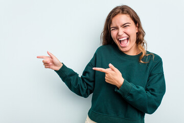 Young caucasian woman isolated on blue background pointing with forefingers to a copy space, expressing excitement and desire.