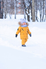 Fototapeta na wymiar Portrait of toddler 15-20 months old in yellow warm clothes walking in a winter park