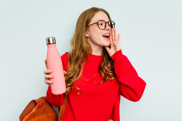 Young student woman holding a canteen isolated on blue background shouting and holding palm near opened mouth.