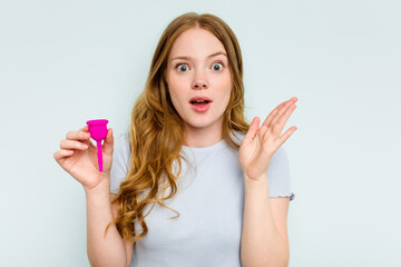 Young caucasian woman holding menstrual cup isolated on blue background surprised and shocked.