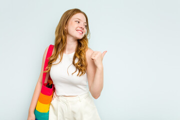 Young caucasian woman holding LGTBI bag isolated on blue background points with thumb finger away, laughing and carefree.